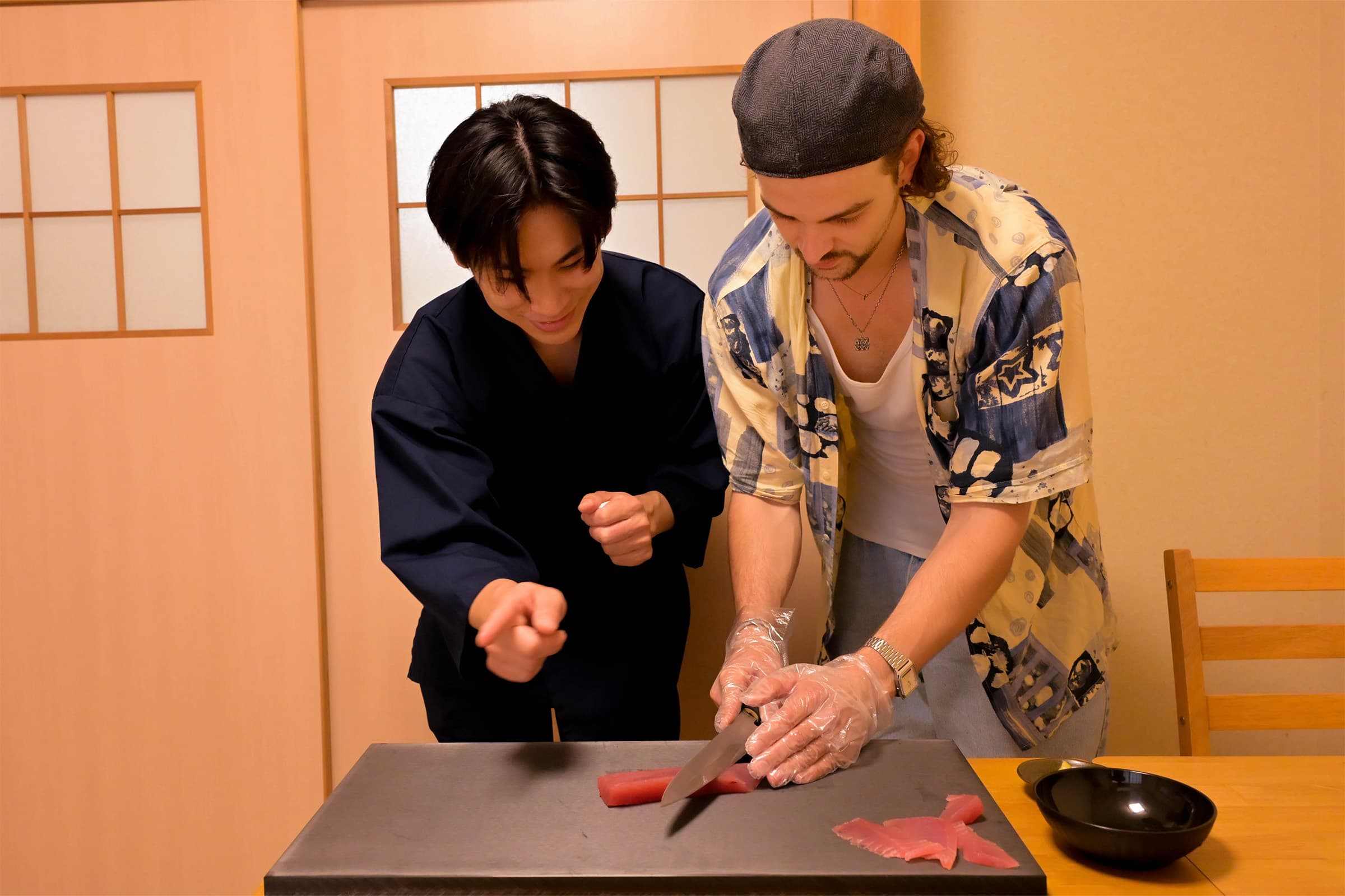 Host guiding a guest as he cuts fresh tuna, in a traditional Kyoto room